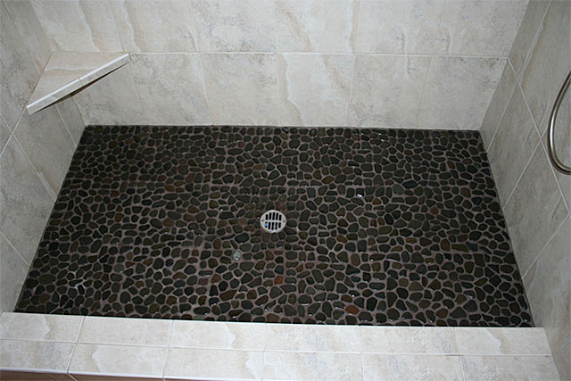 Walk-in shower with dark pebble stone floor and corner bench